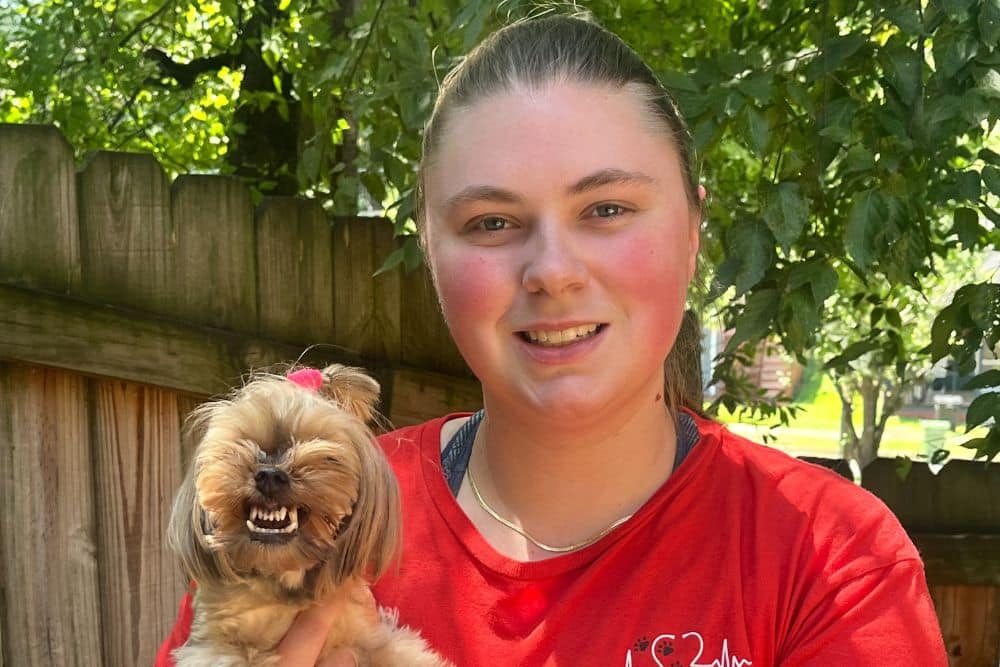 A woman in a red shirt holds a small dog